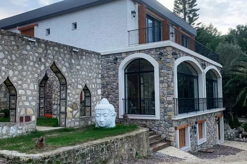 The stone and white main building at Çeşmeköy, with arched windows and a Buddha head sculpture on the lawn