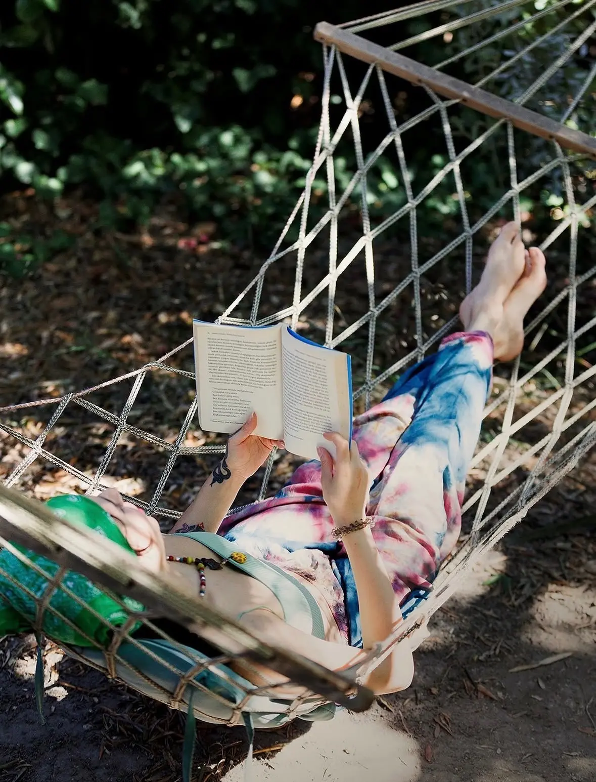 A retreat guest reading a book in a rope hammock in the dappled shade
