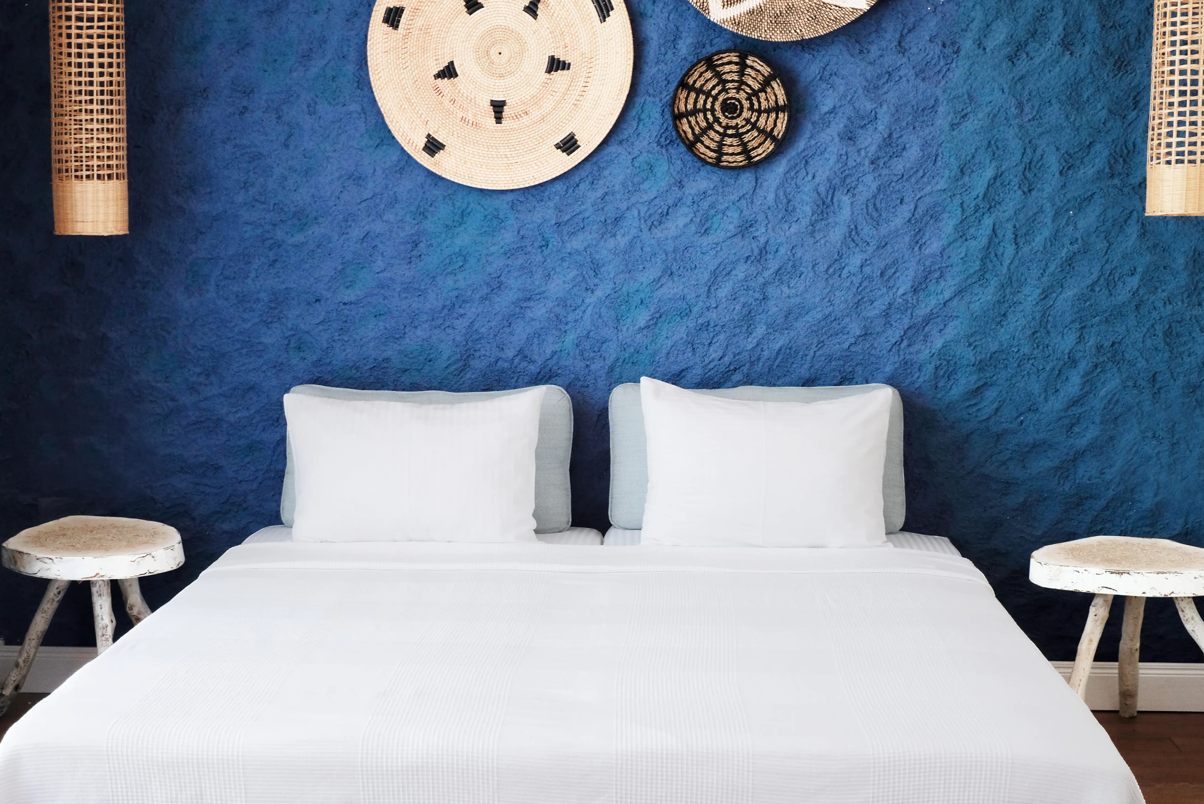 Terrace room with a double bed against a blue textured wall and woven wall discs