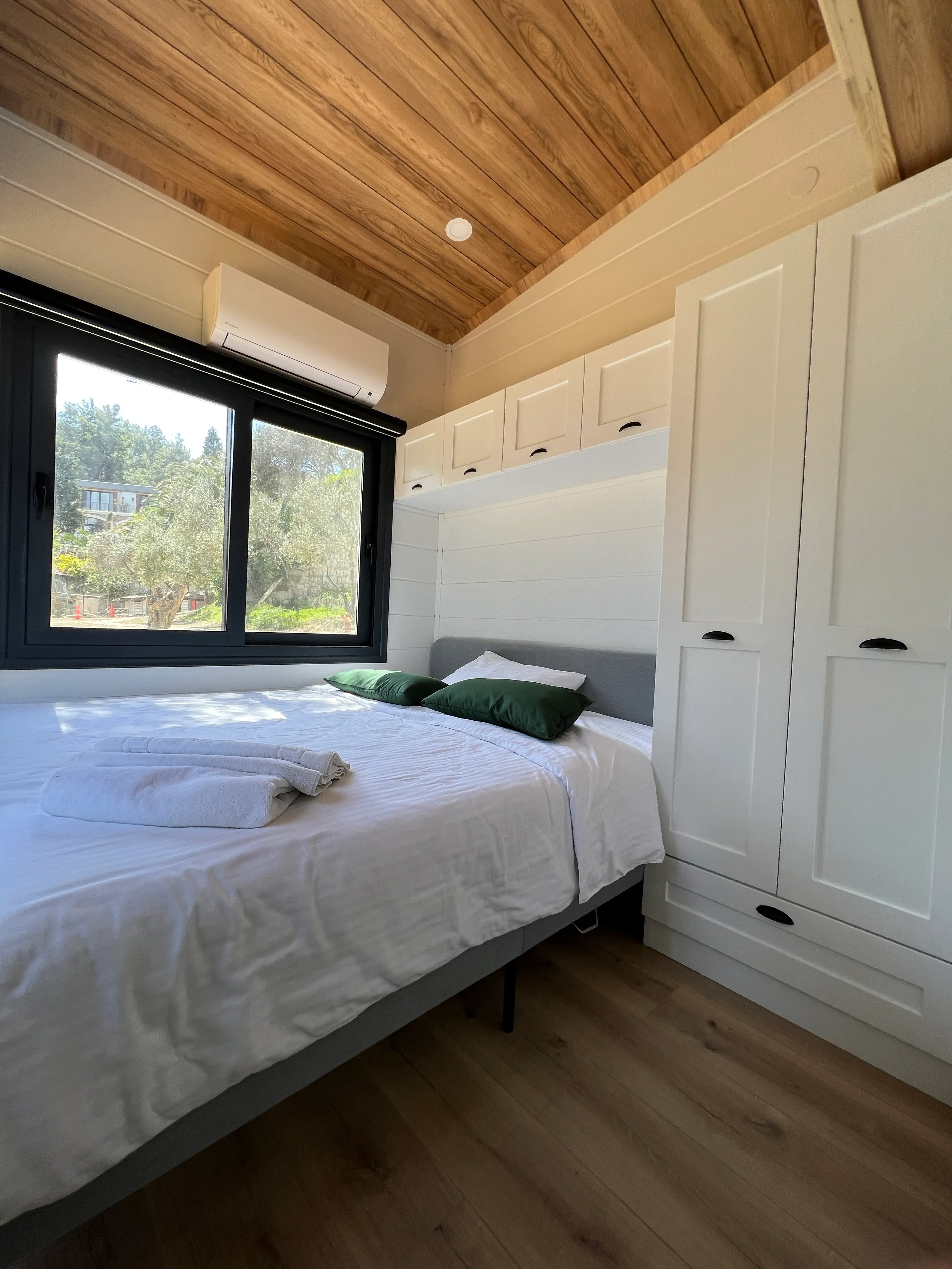 Tiny house bedroom with a double bed and a window onto the olive grove